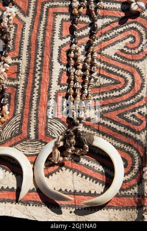 Papouasie-Nouvelle-Guinée, Tufi. Colliers de coquillages avec défenses de sanglier sur tissu traditionnel de tapa fait à la main, en papier mûrier, peint à la main avec natur Banque D'Images