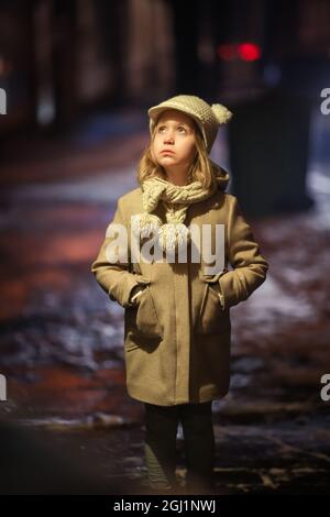 Une petite fille se tient dans la rue à la lumière d'une lanterne le soir par temps froid Banque D'Images