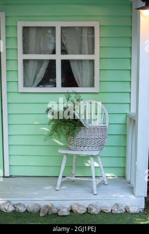 Terrasse confortable avec chaise et panier avec fleurs. Décorations dans le patio pour se détendre. décor d'automne sur la maison porche. Porche extérieur maison avec mobilier de jardin. Banque D'Images