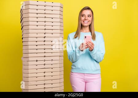 Portrait de fille gaie attrayante avec des boîtes de pile en utilisant le gadget vendre l'achat isolé sur fond jaune vif de couleur Banque D'Images