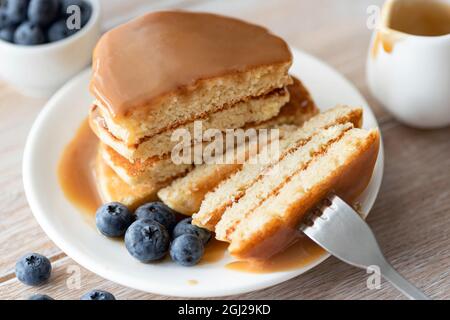 Couper la pile de crêpes avec de la sauce caramel et des bleuets sur l'assiette Banque D'Images