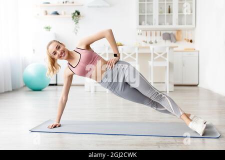 Bonne caucasienne belle blonde millénaire forme physique Blogger dame faisant l'exercice côté planche sur le tapis à la maison seul, espace vide. Soins du corps, crache domestique Banque D'Images