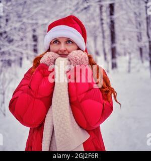 Une femme souriante s'encadre dans des vêtements qui se réchauffent dans une forêt d'hiver avec des arbres dans la neige Banque D'Images