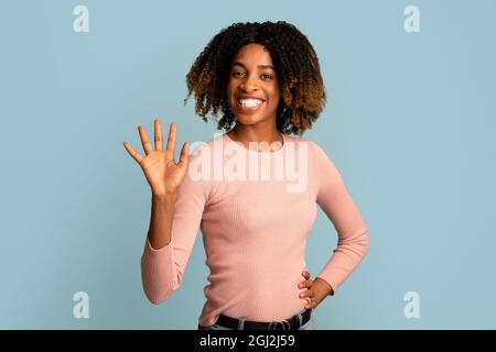Bonjour. Joyeuse amicale jeune afro-américaine agitant la main à la caméra, heureuse souriante noire Millenium femme saluant quelqu'un, en disant Salut pendant Banque D'Images