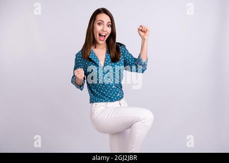 Photo de la jeune femme heureuse impressionnée habillée de blouse bleue souriante Rising Fists isolé de couleur grise fond Banque D'Images