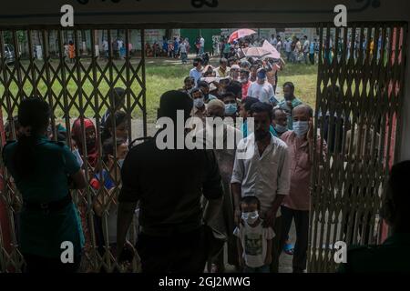 Un policier se tient aux portes et régule le flux de personnes qui recevront le vaccin Moderna Covid-19 lors d'une campagne de vaccination dans un centre de vaccination de Dhaka.les résidents du Bangladesh se réunissent en grand nombre à l'école primaire du gouvernement de Mohammadpur, Un centre de vaccination désigné à Dhaka recevra une dose de vaccin Covid-19, un deuxième jour dans la campagne de vaccination de masse qui a commencé le 7 septembre et se terminera le 12 septembre. (Photo de Sazzad Hossain / SOPA Images / Sipa USA) Banque D'Images