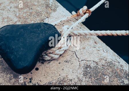 Bollard noir avec corde nouée au bord de la mer, photographié dans un port espagnol Banque D'Images