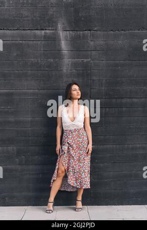 Brunette femme dans des vêtements élégants posant contre un mur noir à l'extérieur dans la rue. Banque D'Images