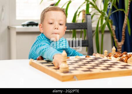 Mignon enfant de 7 ans jouant aux échecs à la maison sur une table en bois blanc. Mise au point sélective. Gros plan. Portrait Banque D'Images