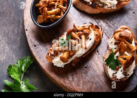 Sandwichs chanterelle au fromage. Sandwich ouvert avec fromage crémeux, assaisonnements, poivre et persil frais sur un fond de bois ancien. Faux Banque D'Images