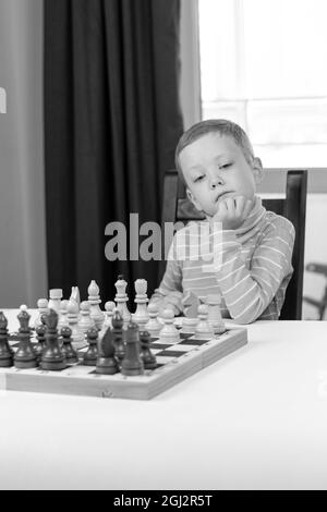 Mignon enfant de 7 ans jouant aux échecs à la maison sur une table en bois blanc. Mise au point sélective. Gros plan. Portrait Banque D'Images