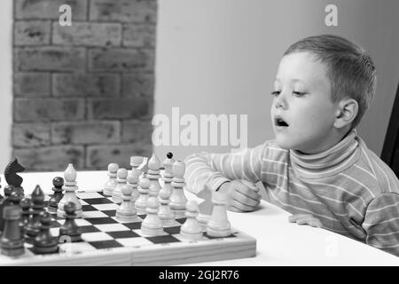 Mignon enfant de 7 ans jouant aux échecs à la maison sur une table en bois blanc. Mise au point sélective. Gros plan. Portrait Banque D'Images