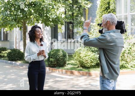 caméraman pointant du doigt près d'un journaliste afro-américain heureux avec microphone Banque D'Images
