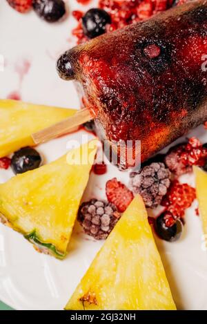 Gros plan de la popsicle de fruits maison sur une assiette avec des baies congelées et des tranches d'ananas Banque D'Images