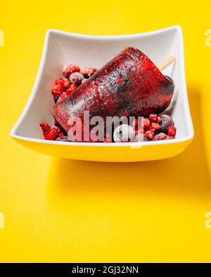 Popsicle de baies maison dans un bol blanc avec baies congelées sur fond jaune Banque D'Images