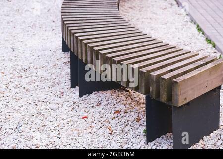 Banc en bois moderne incurvé dans un parc public ou une rue avec chemin en pierres blanches floues sur l'arrière-plan.Focus sur le premier plan. Banque D'Images