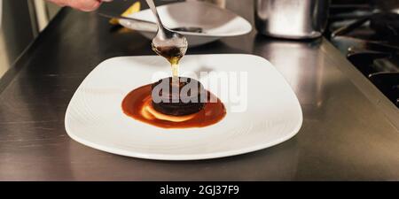 Chef mettant la touche finale sur la plaque de dessert tout en travaillant dans une cuisine de restaurant. Banque D'Images