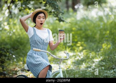 femme asiatique stupéfait de café à emporter et de vélo en regardant loin dans le parc Banque D'Images