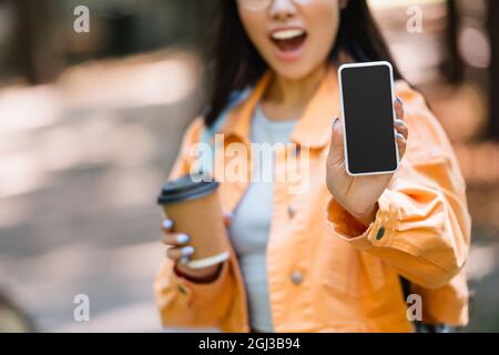 vue rognée d'une femme floue avec une tasse en papier montrant un smartphone avec écran vide en plein air Banque D'Images