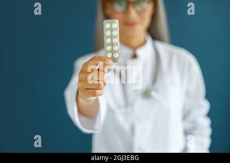 Femme mature dans le manteau se tient sur fond bleu, se concentrer sur la main avec blister de pilules Banque D'Images