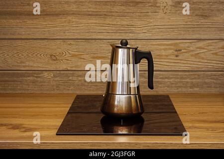 Geyser machine à café sur le panneau de chauffage électrique de la cuisinière sur le fond d'un mur en bois. Banque D'Images