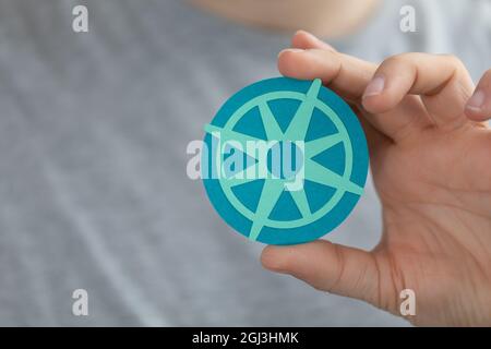Gros plan de la main d'un homme caucasien alors qu'il tient une petite découpe de papier bleu d'un compas Banque D'Images