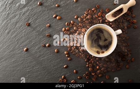 Tasse blanche avec café chaud avec mousse et grains torréfiés chauds sur table en ardoise. Vue de dessus. Composition horizontale. Banque D'Images