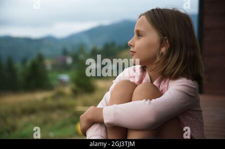 Petite fille blonde assise à l'extérieur et regardant la vue Banque D'Images