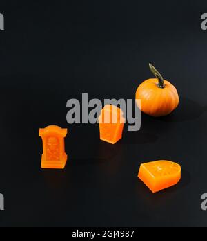 Trois pierres tombales orange et une citrouille orange sur fond noir. Concept créatif Halloween sombre effrayant. Banque D'Images