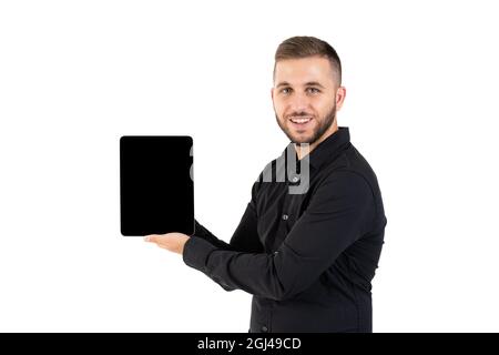 Jeune homme avec une chemise noire montrant une tablette à écran noir sur fond blanc Banque D'Images