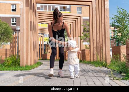 bébé fille avec maman marchant dans la cour de la ville, l'enfant apprend à marcher Banque D'Images