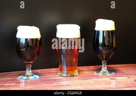 Trois verres différents avec trois bières sombres différentes, le bière, le ravin et le bock, sont placés dans une rangée sur une table en bois. Gros plan. Banque D'Images