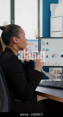 Une femme d'affaires multitâche qui parle sur une ligne fixe explique les graphiques de l'entreprise à une collegue à distance tout en ayant une commande de repas à emporter à la réception. Directeur mangeant une tranche de pizza de dégustation Banque D'Images
