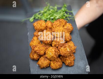 Délicieux plat de petits-en-cas de cuisine asiatique à base d'oignons bhaji lors de la réception de mariage. Sur l'ardoise tenue par la serveuse de la ferme de nourriture fraîche hors-d'œuvre cuite. Banque D'Images