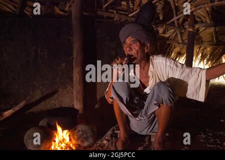 Homme birman local fumant un cigare par le feu dans sa maison à Bagan, Myanmar. Banque D'Images