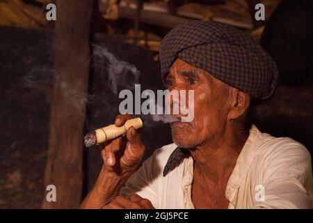 Homme birman local fumant un cigare par le feu dans sa maison à Bagan, Myanmar. Banque D'Images