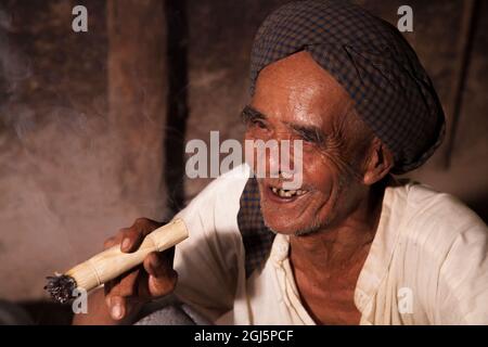 Homme birman local fumant un cigare par le feu dans sa maison à Bagan, Myanmar. Banque D'Images