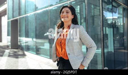 femme d'affaires riant joyeusement et regardant la caméra tout en se tenant devant un immeuble de bureaux de grande hauteur dans la ville. Entrée femelle réussie Banque D'Images