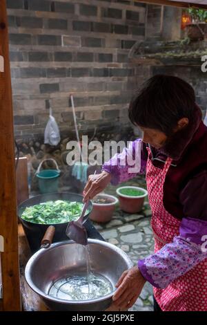 Chine, province de Fujian, Nanjing, Huaiyuan Tulou. Une femme prépare de la soupe au centre de la maison ronde où se trouve la cuisine. (Usage éditorial uniquement) Banque D'Images
