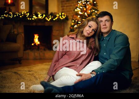 Beau couple caucasien d'âge moyen posant à l'intérieur de noël avec un arbre de noël et des guirlandes. Mise au point douce sélective, effet de grain de film Banque D'Images