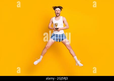 Vue sur toute la longueur de la taille du corps d'un sympathique gars sportive jumping tenant la tasse isolée sur fond jaune vif Banque D'Images