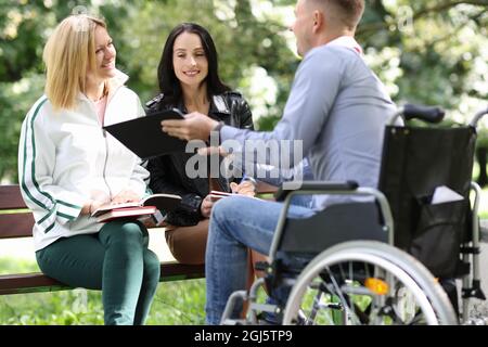 Un homme handicapé en fauteuil roulant montre les résultats de son travail de designer sur tablette aux femmes dans le parc Banque D'Images