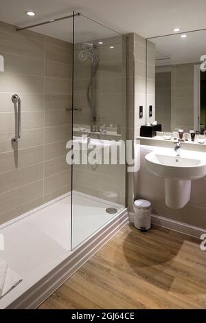 Moderne, cabine de douche carrelée et écran, grande poignée de sécurité dans la salle de bains de l'hôtel, miroir pleine hauteur sur le mur, lavabo, Angleterre, Royaume-Uni Banque D'Images