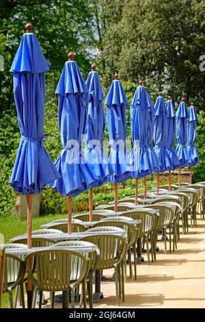 Une rangée de chaises de table extérieures et de parasols bleus repliés à l'extérieur du bar de l'hôtel, où le temps est trop froid et trop venteux pour les clients en mai Angleterre au Royaume-Uni Banque D'Images