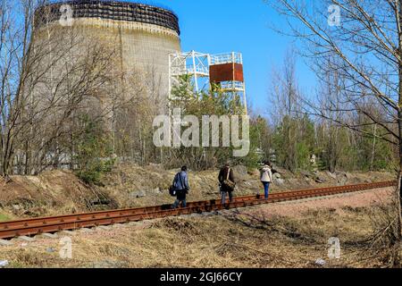 Ukraine, Pripyat, Tchernobyl. Les touristes marchant le long des voies ferrées près de la tour de refroidissement inachevée pour les réacteurs 5 et 6 qui n'ont jamais été achevés. (E Banque D'Images