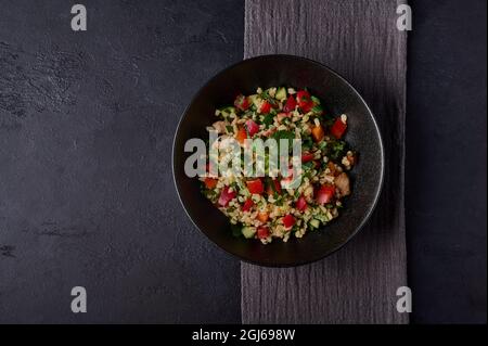 Tabouleh à salade traditionnel composé de bulgur ou de couscous, viande de volaille, persil, menthe dans un bol sombre avec serviette sur fond noir Banque D'Images