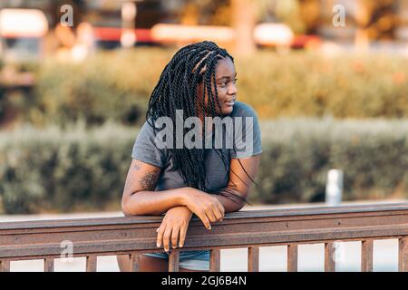 Femme afro distraite avec des cheveux tressés penchée sur un rail dans la rue Banque D'Images