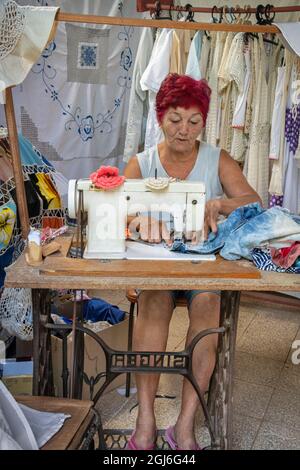 Femme avec des cheveux rouges coudre des vêtements et des poupées farcies pour vendre des touristes de la porte de sa maison à Trinidad, Cuba Banque D'Images