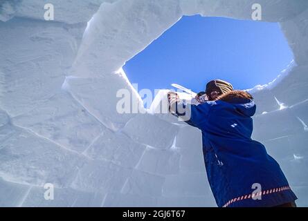 Baker Lake, Nunavut, Canada. Homme aîné inuit, habillé de vêtements modernes de l'arctique, construisant des igloo en sculptant des blocs de neige et en les plaçant soigneusement. THI Banque D'Images
