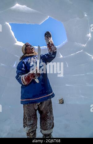 Baker Lake, Nunavut, Canada. Homme aîné inuit, habillé de vêtements modernes de l'arctique, construisant des igloo en sculptant des blocs de neige et en les plaçant soigneusement. THI Banque D'Images